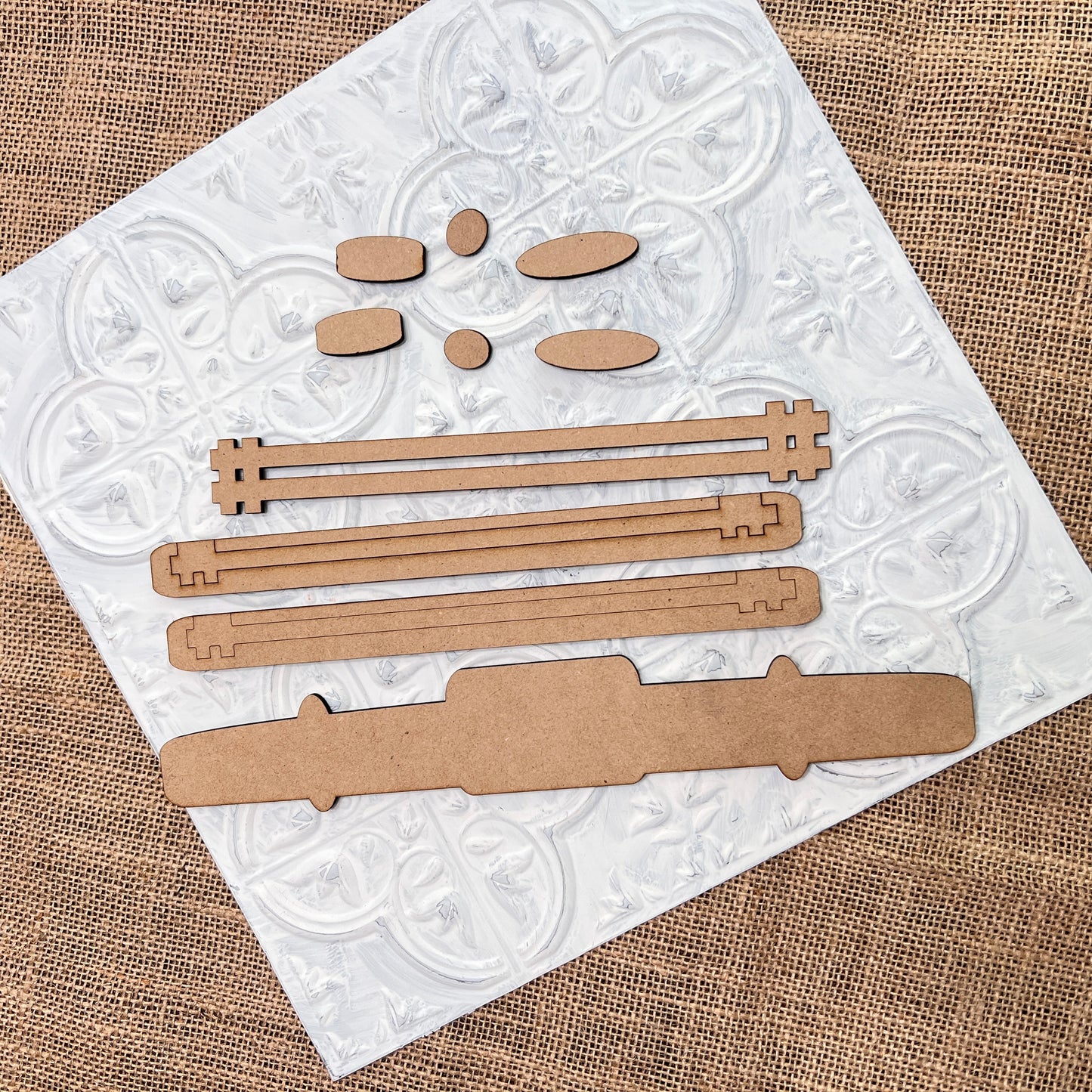 Janet's Craft Corner's Antique Truck Base Double-Sided Add-On DIY craft kit set is arranged on a textured white tile over burlap, perfect for creating or customizing truck-themed accessories.
