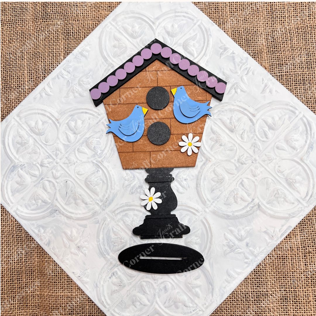 A completed DIY birdhouse kit featuring birds and daisies on a textured white background.