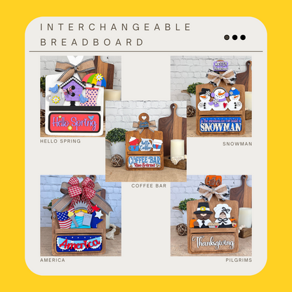 The image showcases Janet's Craft Corner's DIY Breadboard Interchangeable Base with Insert. This home decor kit includes themed designs—"Hello Spring," "Coffee Bar," "Snowman," and "Thanksgiving"—each with colorful decorations, ideal for adding a festive wooden touch to your decor.