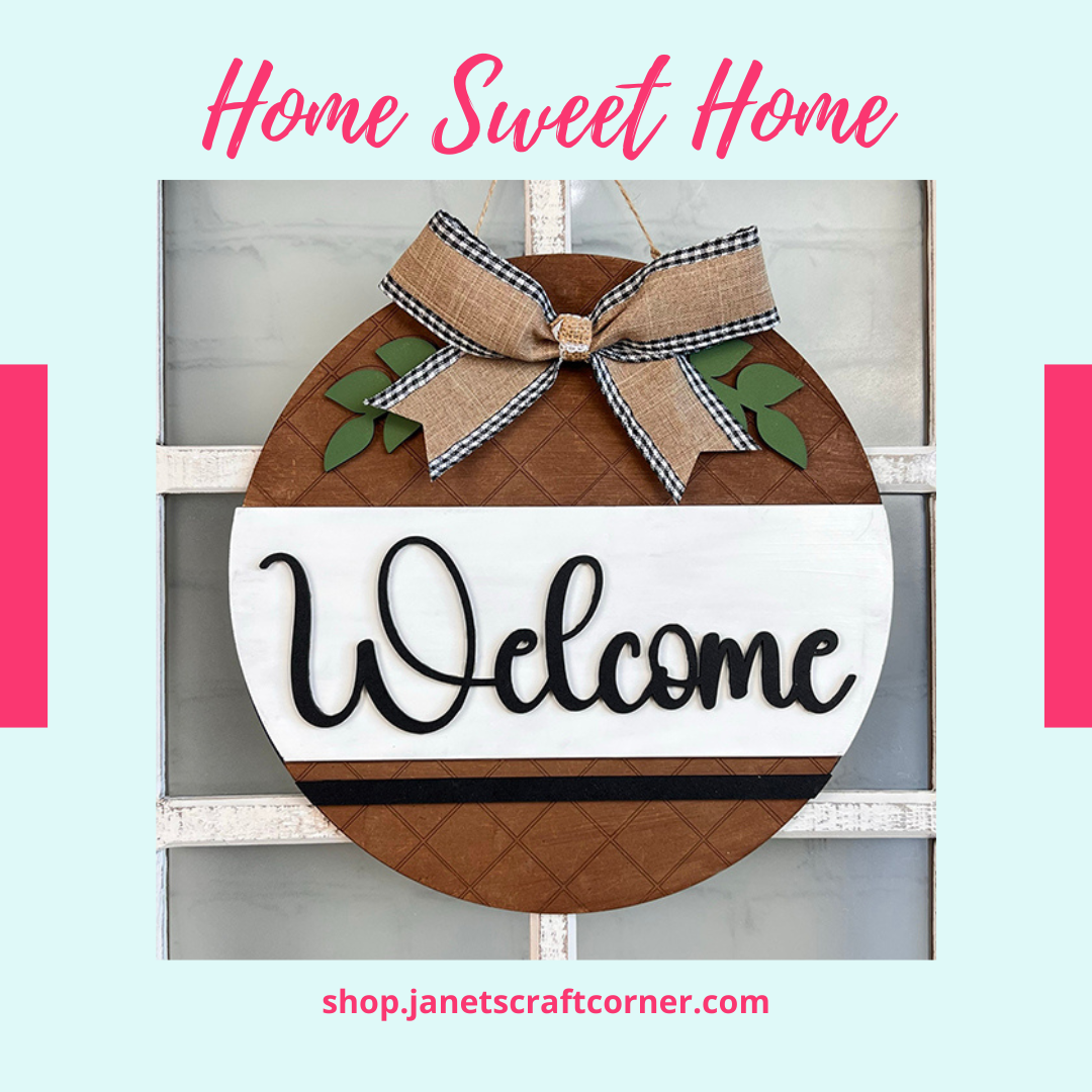 Janet's Craft Corner's Welcome Round Door Hanger is a farmhouse decor kit featuring "Welcome" in bold script on a brown textured background, with a checkered burlap bow and green leaves. It includes "Home Sweet Home" above—perfect for your DIY home decor needs.