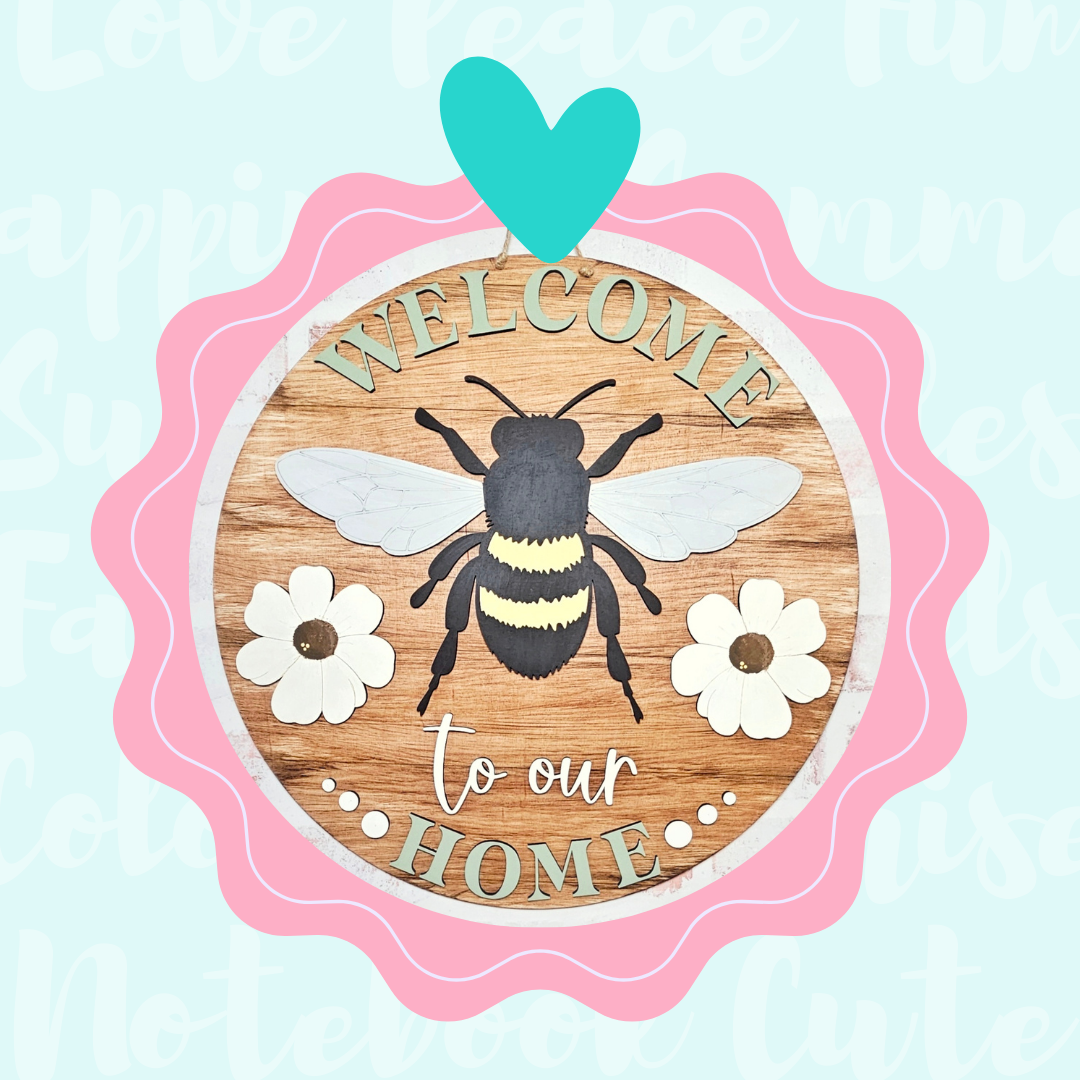 The DIY Welcome Home Bees & Blooms Sign from Janet's Craft Corner features a bee and flowers with "Welcome to our Home" text, a pink and teal scalloped border, and pastel background words, making it an adorable door hanger for any entryway.