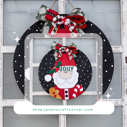 Adorn your festive wreath with the Jolly Santa Round Sign from Janet's Craft Corner. Featuring red and black ribbons and holly, it's perfect for holiday decor on a white rustic door. Explore more at shop.janetscraftcorner.com.