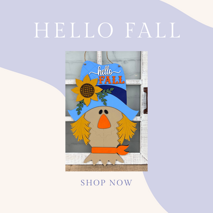 Illustration of a scarecrow with a blue hat and a sunflower, featuring "Hello Fall" text. The pastel backdrop reads "HELLO FALL" at the top and "SHOP NOW" at the bottom. Ideal for those wanting personalized home decor. Product: Scarecrow Door Hanger DIY Kit by Janet's Craft Corner.