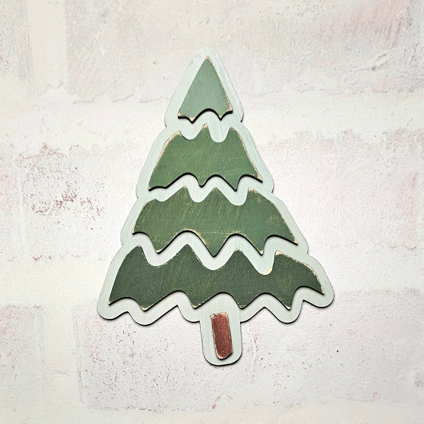 A wooden Christmas tree ornament from Janet's Craft Corner's Trim a Tree Kids Pop-Out Kit rests on a light textured background. The tree, perfect for personalizing holiday décor, features three green tiers with a small brown trunk at the bottom.