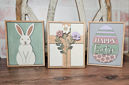 The Easter Bunny Farmhouse Sign by Janet's Craft Corner includes three wood cut-out signs: a rabbit on green, flowers on a wood cross, and a colorful egg with "Happy Easter." This DIY craft kit is ideal for adding seasonal charm to your rustic home decor.