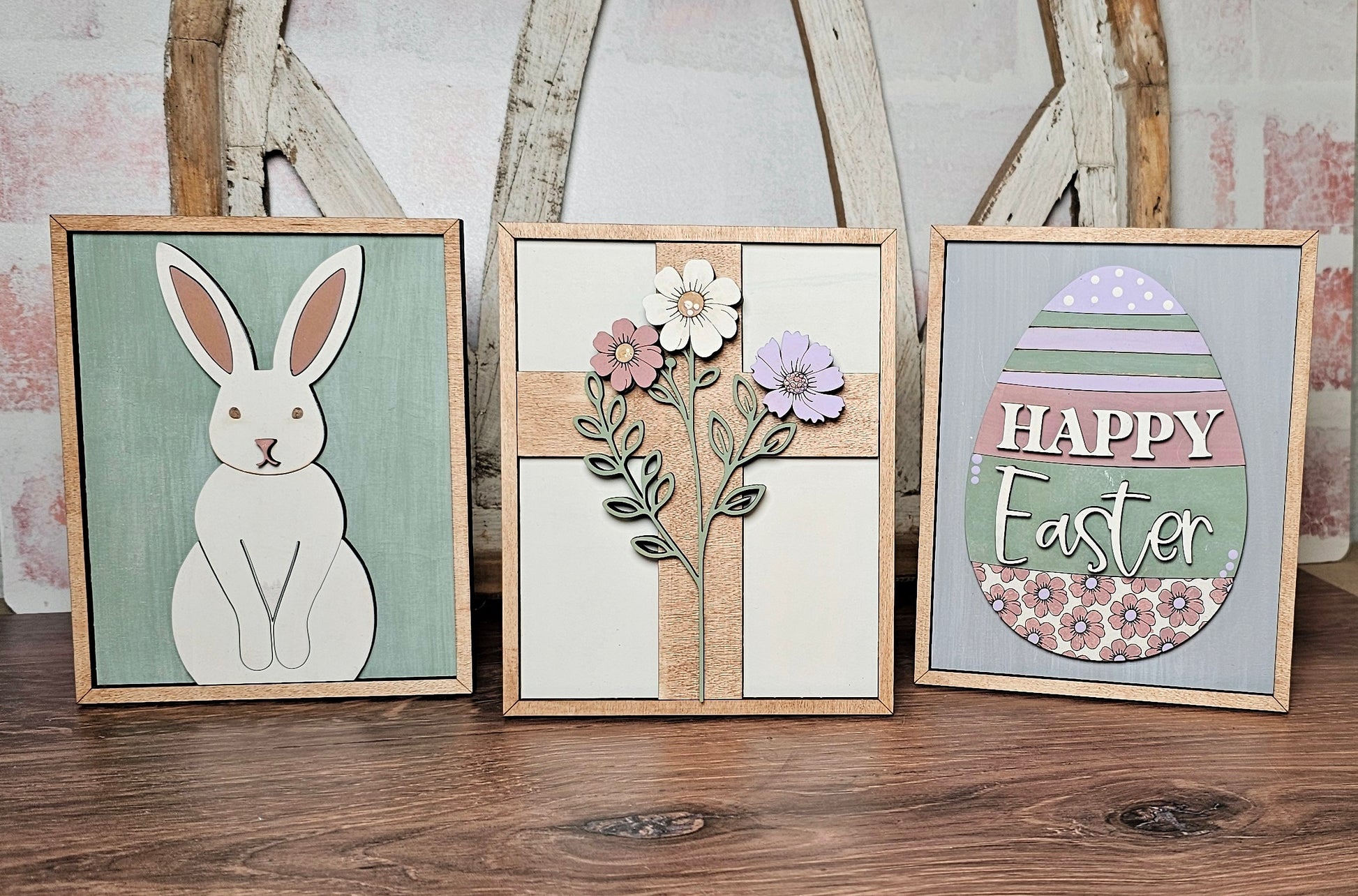 Janet's Craft Corner offers the "Easter Egg Farmhouse Sign," featuring three decorative wooden frames: a white rabbit on green, cross-shaped flowers, and an Easter egg with "Happy Easter" text. These are perfect as DIY seasonal decor to enhance your festive spirit with crafty charm.