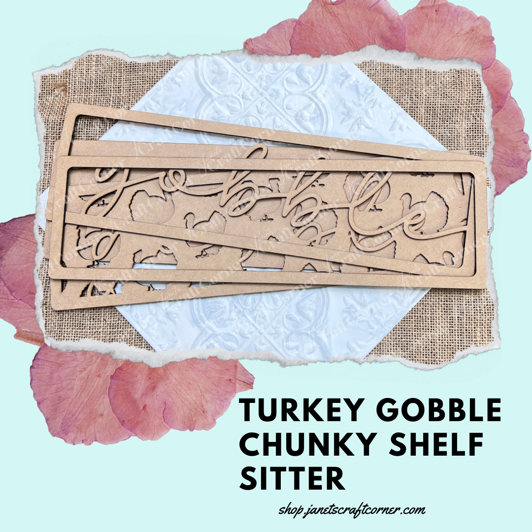 The "Gobble Turkey Chunky Shelf Sitter" from Janet's Craft Corner features a hand-painted wooden design on textured paper, adorned with pink petals and set against a turquoise backdrop. Ideal for seasonal home decor, visit shop.jenscraftscorner.com for more delightful finds.