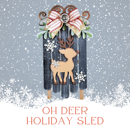 The Oh Deer Sled Wall Hanger by Janet's Craft Corner features a festive sled with a reindeer cutout and white snowflakes on a snowy background, accented with a red and white ribbon and button. Perfect for DIY seasonal home decor.