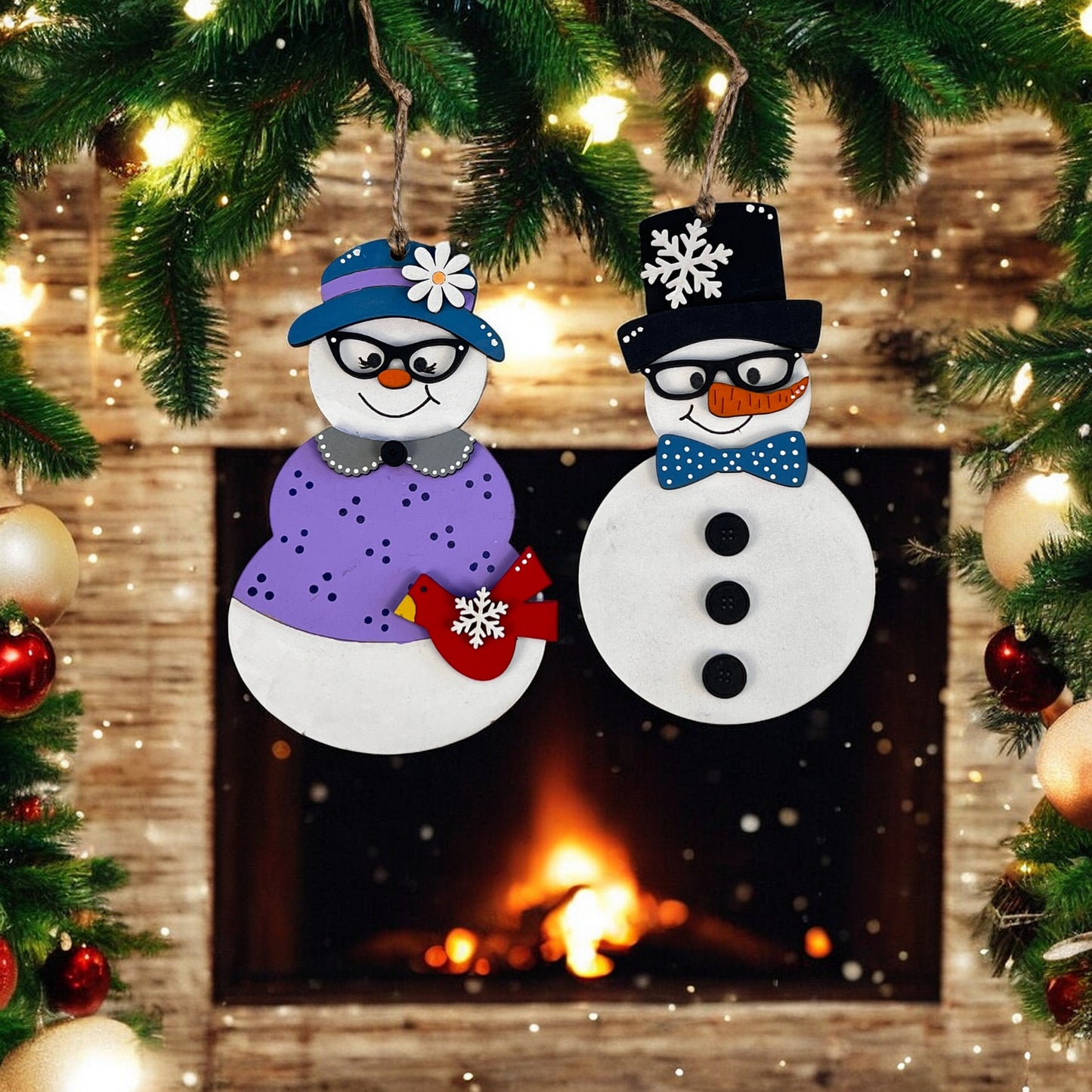 A festive scene features Janet's Craft Corner's Vintage Snow Couple Ornaments, one dressed in a purple outfit with a blue hat and the other in a black top hat and bow tie, all set against a glowing fireplace adorned with festive decorations and twinkling lights.