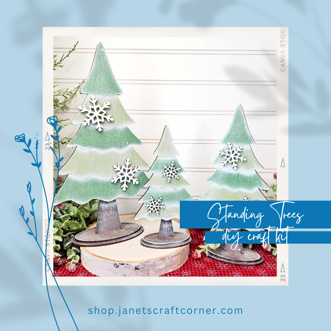 On a table, three wooden craft trees feature green tiers and snowflake decorations. The text reads "Standing Trees - DIY seasonal home decor craft kit - Set of 3" by Janet's Craft Corner, an ideal addition to your home. A floral-accented blue background holds a web link at the bottom.