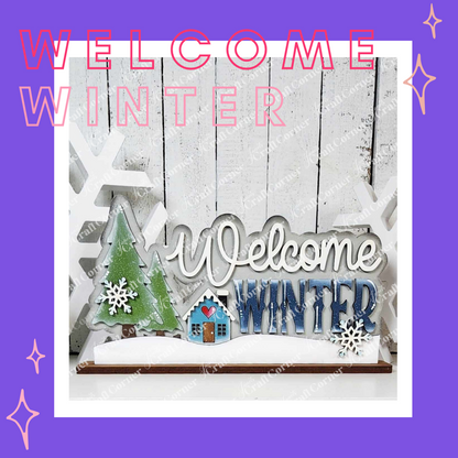 The "Welcome Winter" Word Art Shelf Sitter by Janet's Craft Corner is a DIY craft kit for festive home decor. This hand-painted sign features a tree, snowflakes, and a snow-covered house on a white background with decorative stars against a purple border.