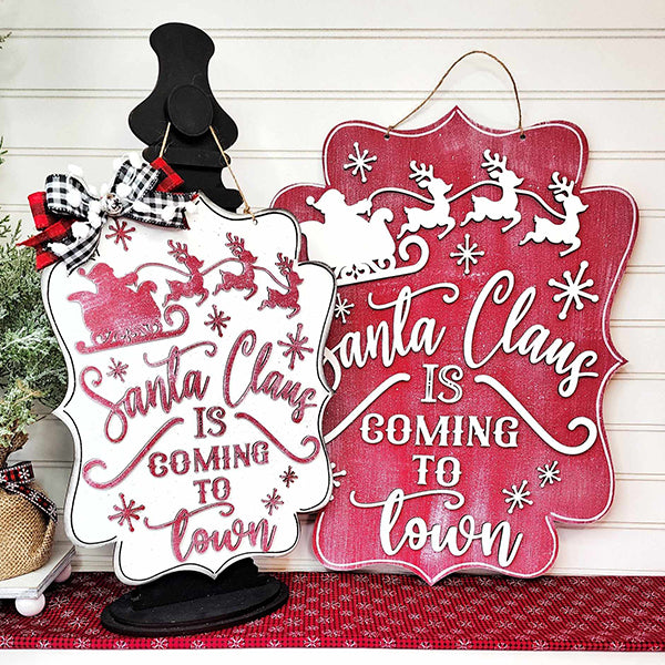 Discover the perfect festive touch with Janet's Craft Corner's "Santa is Coming to Town Door Hanger." This charming set includes two designs: one with a white base, adorned with red glitter and supported by a black stand, and the other showcasing holly and decorative bows as it leans elegantly against a white wall. Both feature iconic motifs of Santa’s sleigh and reindeer, making them ideal for spreading holiday spirit as delightful door decorations.