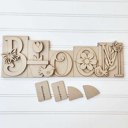 Introducing the "Bloom Word Block Shelf Sitter" from Janet's Craft Corner. This DIY home decor kit features a wood sign with carved letters: butterfly on "B," tulip on "L," bird on "O," flower on the second "O," and leaves with a bird on "M." Easy to assemble for seasonal decor.