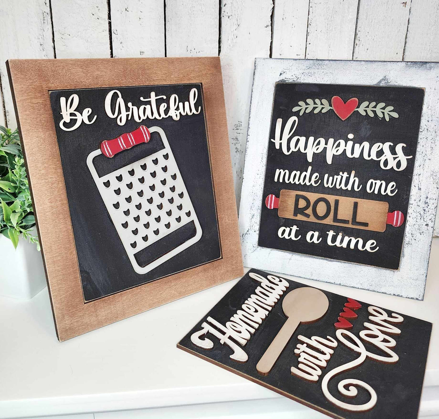 Janet's Craft Corner offers a Simple Farmhouse Frame for Interchangeable Signs - a DIY Home Decor Craft Kit. It includes "Be Grateful" with a grater, "Happiness made one roll at a time" with a rolling pin, and "Homemade with Love" featuring a spoon—a charming addition to any kitchen.