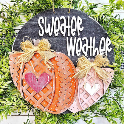 Introducing the Sweater Pumpkin Door Hanger DIY home decor craft kit by Janet's Craft Corner. This charming decorative sign, titled "sweater weather," showcases two pumpkin shapes embellished with bows. It is hand-painted in vibrant autumn hues and surrounded by green leaves, making it a welcoming piece of personalized home decor.