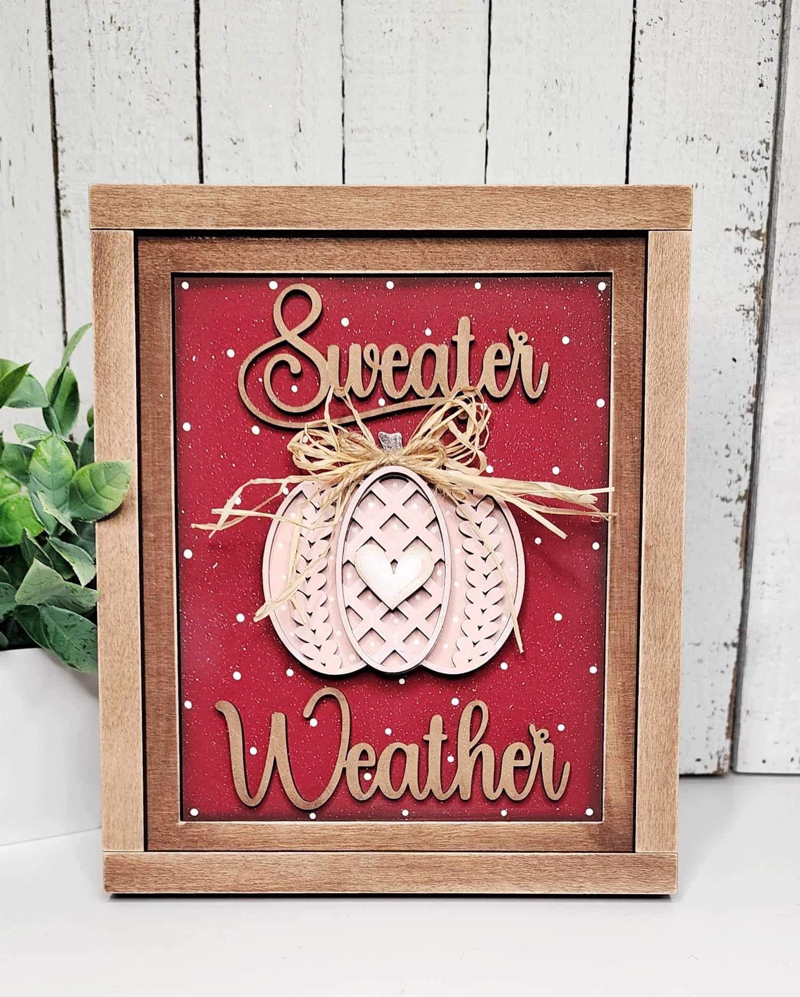 Janet's Craft Corner offers a DIY home decor kit featuring a wooden farmhouse frame with the cursive "Sweater Weather." It showcases a decorative pumpkin with a bow against a red polka-dot background and pairs beautifully with green plants as interchangeable home decor.