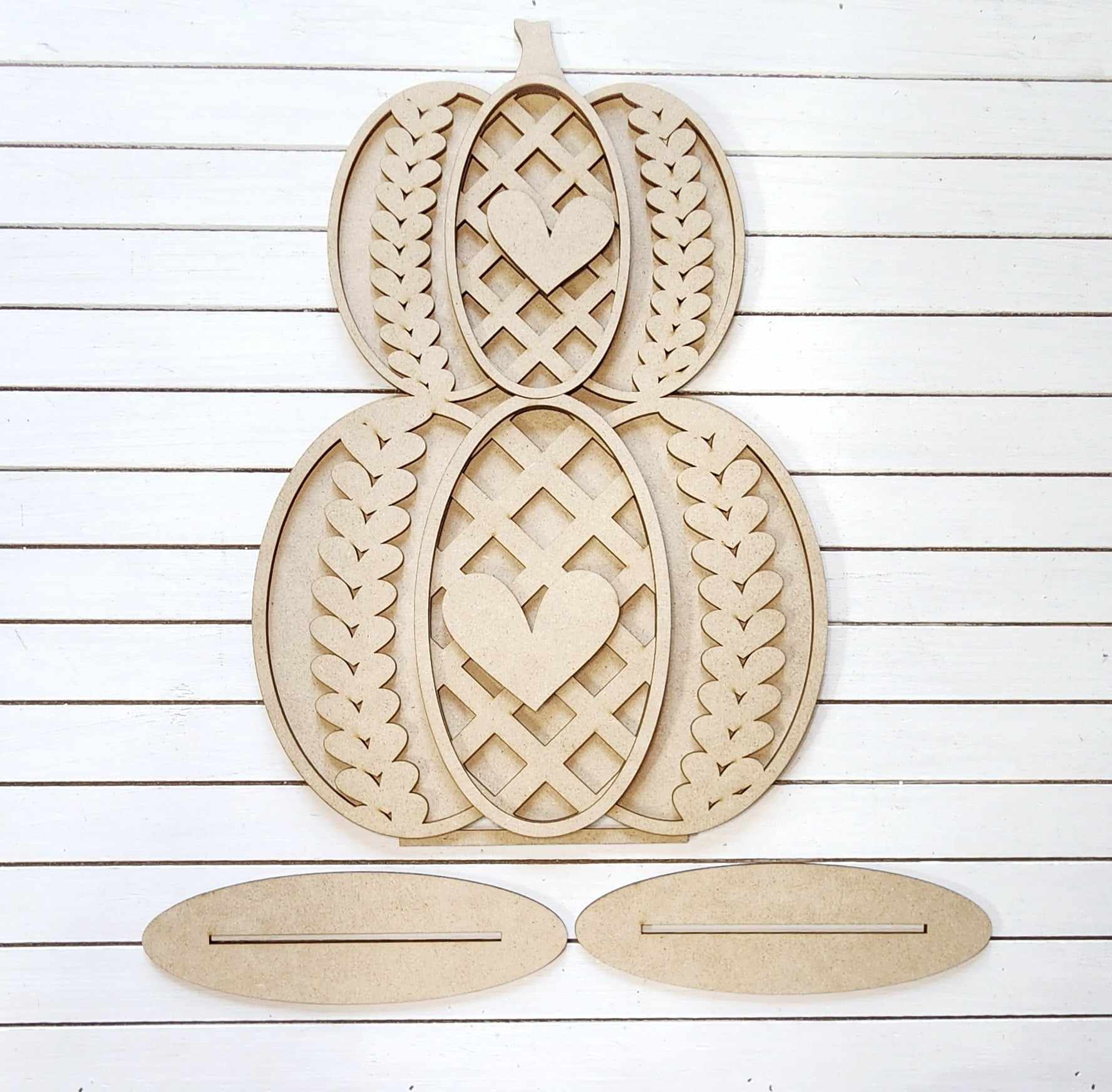 The Sweater Pumpkin Shelf Sitters, part of a DIY home decor craft kit from Janet's Craft Corner, feature an intricate wooden pumpkin cutout design adorned with lattice patterns, hearts, and leaf motifs. Displayed flat against a white wooden background, the set includes two oval base pieces beneath the pumpkin shape, making them ideal for charming home décor projects.