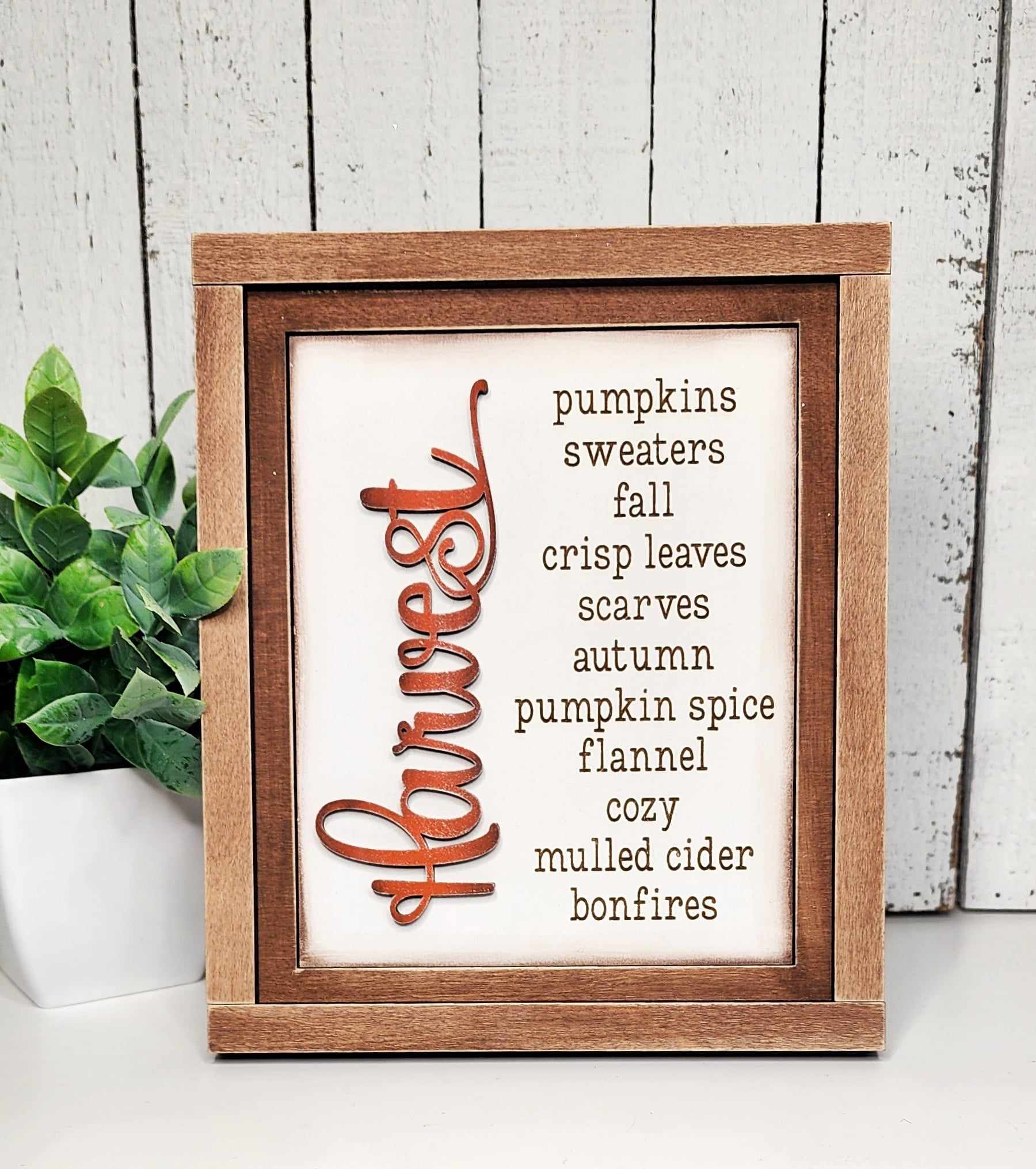 The Farmhouse Frame for Interchangeable Signs by Janet's Craft Corner offers a cozy autumn vibe with fall-themed words like harvest, pumpkins, and crisp leaves. Ideal for decor enthusiasts, this DIY craft kit pairs perfectly with a small potted plant to complete the look.