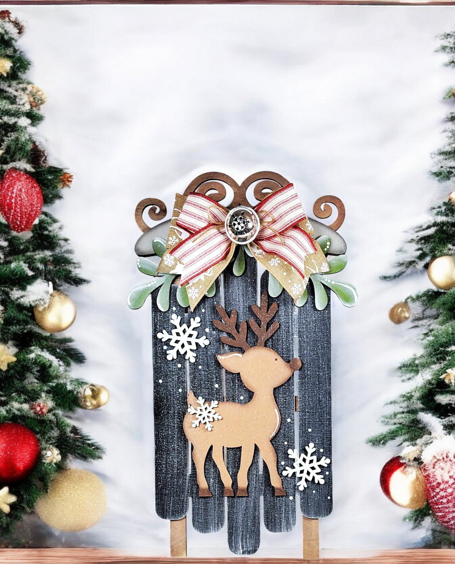 The Oh Deer Sled Wall Hanger from Janet's Craft Corner is a DIY seasonal decor kit including a wooden sled with reindeer cutout, snowflakes, and ribbons. It comes with two Christmas trees decorated in red and gold against a snowy backdrop—ideal for home decor enthusiasts!.