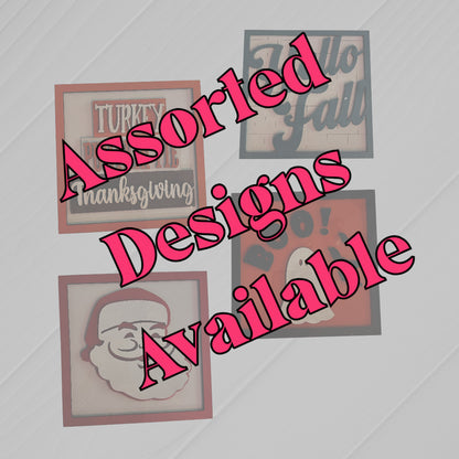 Four 6-inch square holiday cards from Janet's Craft Corner, featuring Thanksgiving, fall, Halloween, and Santa designs. Bold pink text diagonally states "Assorted Designs Available" across the image.