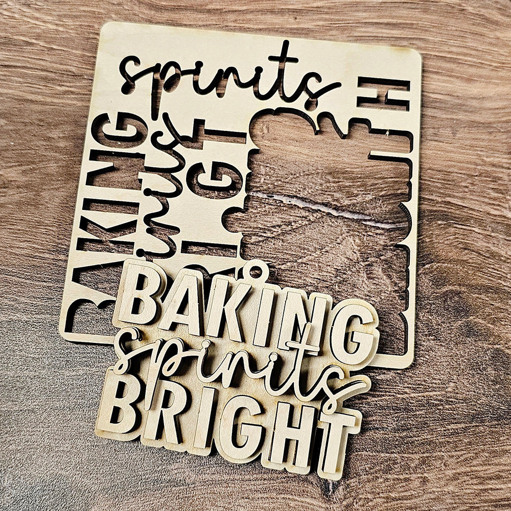 A wooden cutout from the Baking Spirits Bright Ornaments - Set of 4 by Janet's Craft Corner features the phrase "BAKING spirits BRIGHT" in bold letters, with "spirits" elegantly scripted in cursive. It sits on a wooden surface alongside its original frame, making it a charming addition to your holiday decor.