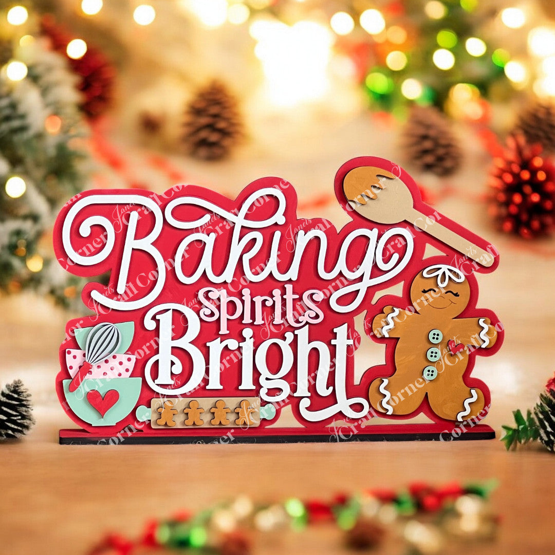 The "Baking Spirits Bright" Shelf Sitter by Janet's Craft Corner features a hand-painted sign with a spoon, gingerbread man, and gift box. Blurred holiday lights and pine branches add warmth—ideal for DIY craft kits or home decor.