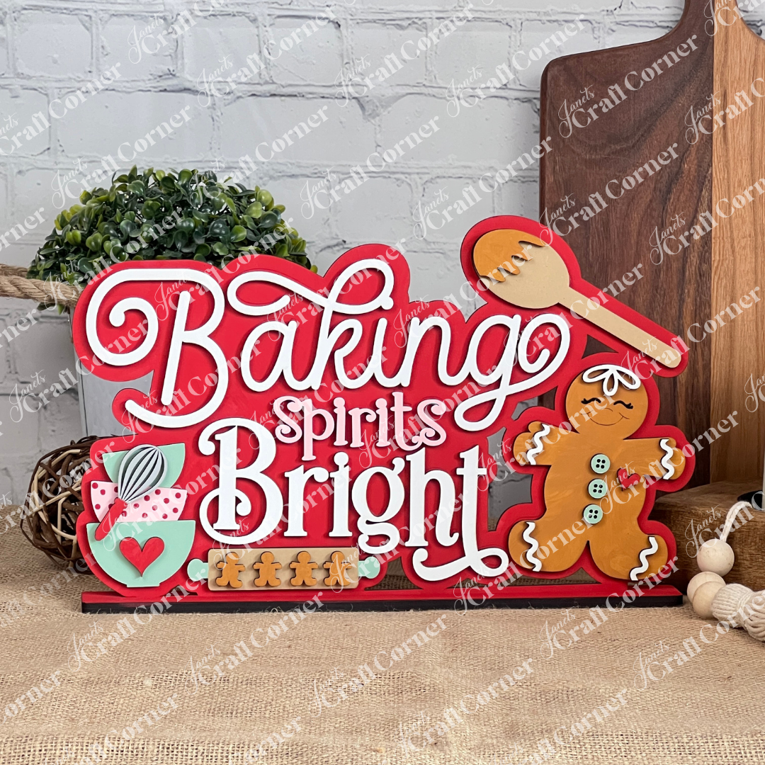 Introducing the "Baking Spirits Bright" Shelf Sitter by Janet's Craft Corner, a delightful DIY home decor craft kit. This festive piece showcases a charming hand-painted sign with the phrase "Baking Spirits Bright" alongside whimsical elements like a gingerbread man, mixing spoon, and mug. Adorned with small gingerbread figures and set against a brick wall backdrop, it's perfect for adding a touch of holiday cheer to your home.