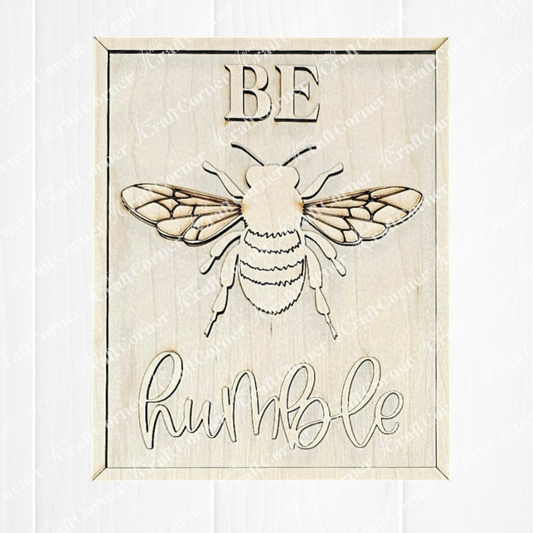 The Be Humble Farmhouse Sign by Janet's Craft Corner is a DIY kit for crafting a wooden art piece. It features a bee illustration with "BE" engraved above and "humble" in cursive below on light wood with natural grain, ideal for farmhouse décor.