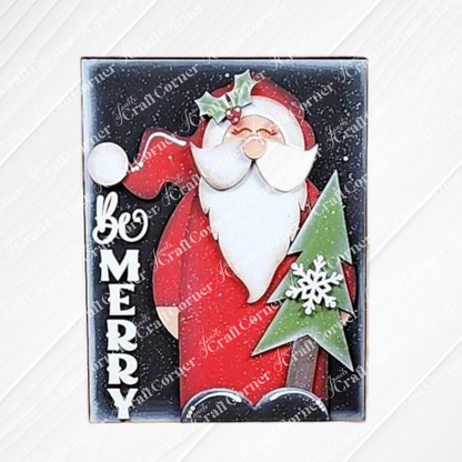 Be Merry Farmhouse Sign by Janet's Craft Corner features an illustration of Santa Claus in a red suit holding a green Christmas tree adorned with a white snowflake. The phrase "Be Merry" is prominently displayed in bold white letters on the left side, making it an excellent choice for interchangeable home decor.