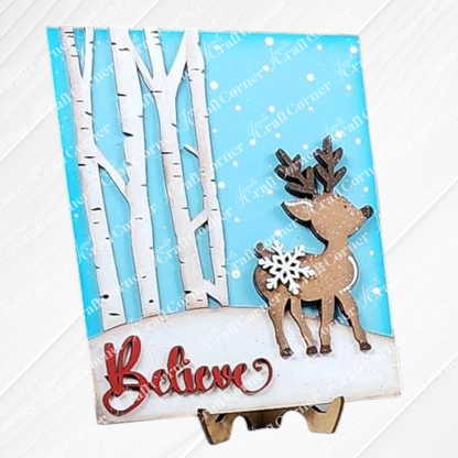 The "Oh Deer Believe Farmhouse Sign" by Janet's Craft Corner is a charming decorative card that showcases a reindeer adorned with a snowflake on its back. The reindeer stands gracefully on snowy ground, set against the backdrop of white birch trees and a blue sky. At the bottom, the word "Believe" is elegantly scripted in red, making it an ideal piece for home decor or as an addition to your DIY craft kit collection.