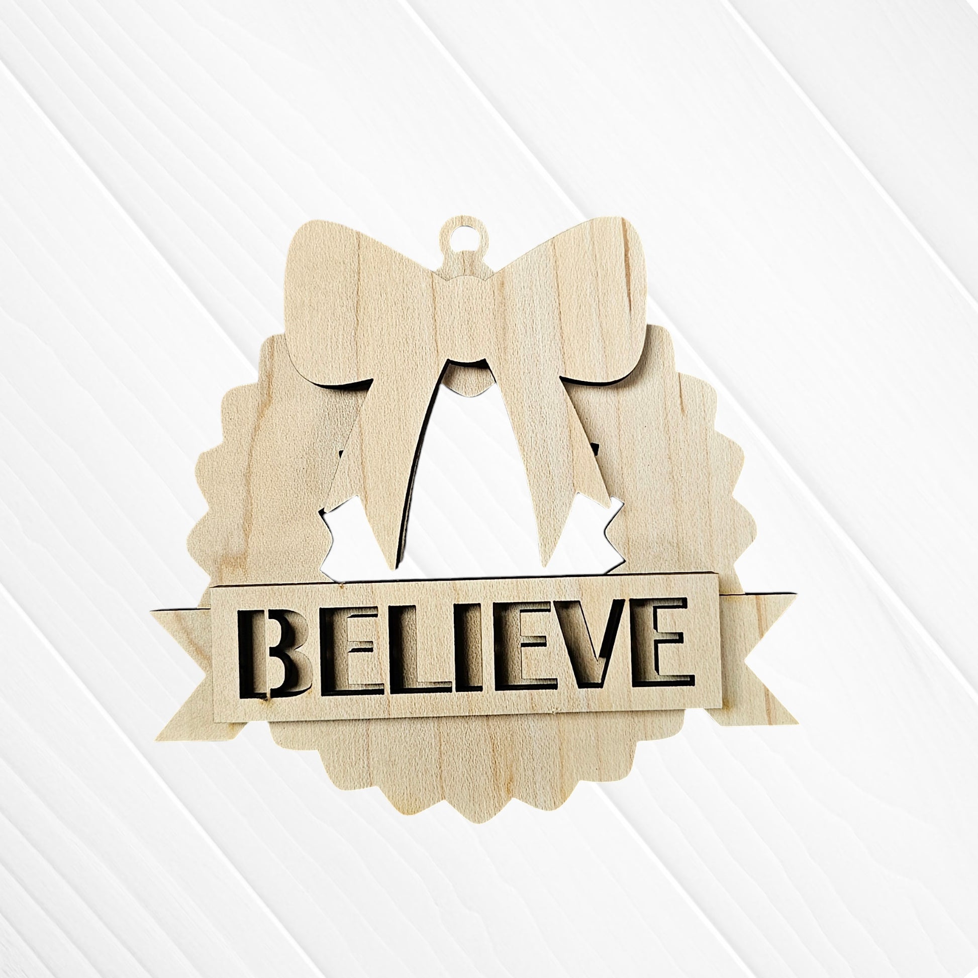 The Holiday Village Ornament Set by Janet's Craft Corner features hand-painted wooden ornaments engraved with "BELIEVE," shaped like a wreath and adorned with a bow. Perfect for your holiday DIY craft kit collection.