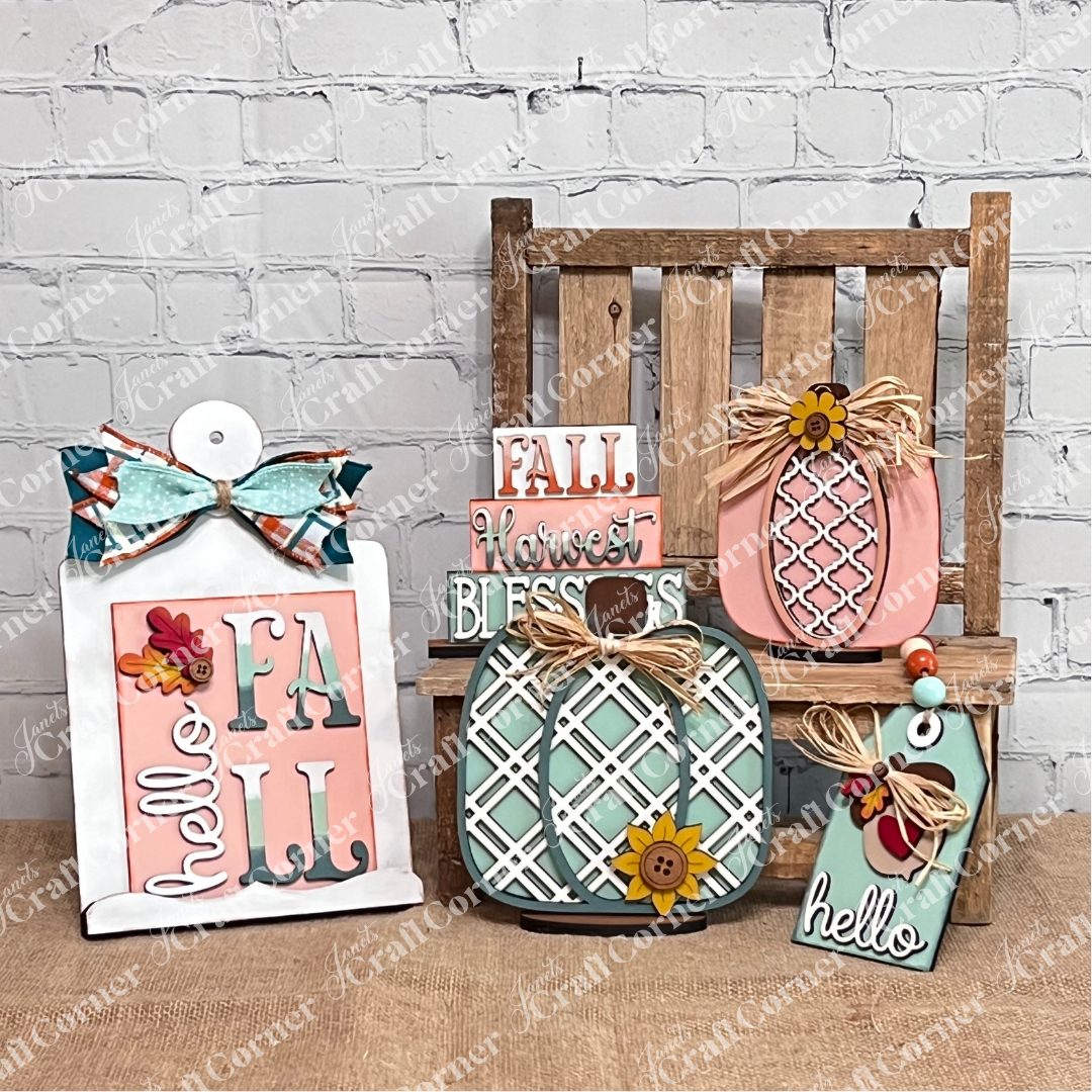 A display of fall-themed wooden decor—pumpkins, flowers, bows, and festive signs from Janet's Craft Corner’s Crafted by You! Subscription DIY home decor kit—styled on a small bench against a white brick wall for autumn craft inspiration.