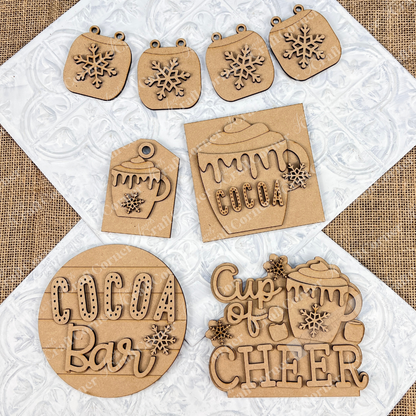 The Cup of Cheer Hot Cocoa Decor Set from Janet's Craft Corner is a DIY home decor craft kit featuring a collection of hand-painted wooden cutouts with holiday-themed designs, such as snowflakes, a "Cocoa" mug, and the phrases "Cocoa Bar" and "Cup of Cheer." Perfect for adding festive charm to your home, these pieces are beautifully displayed on a textured white surface.