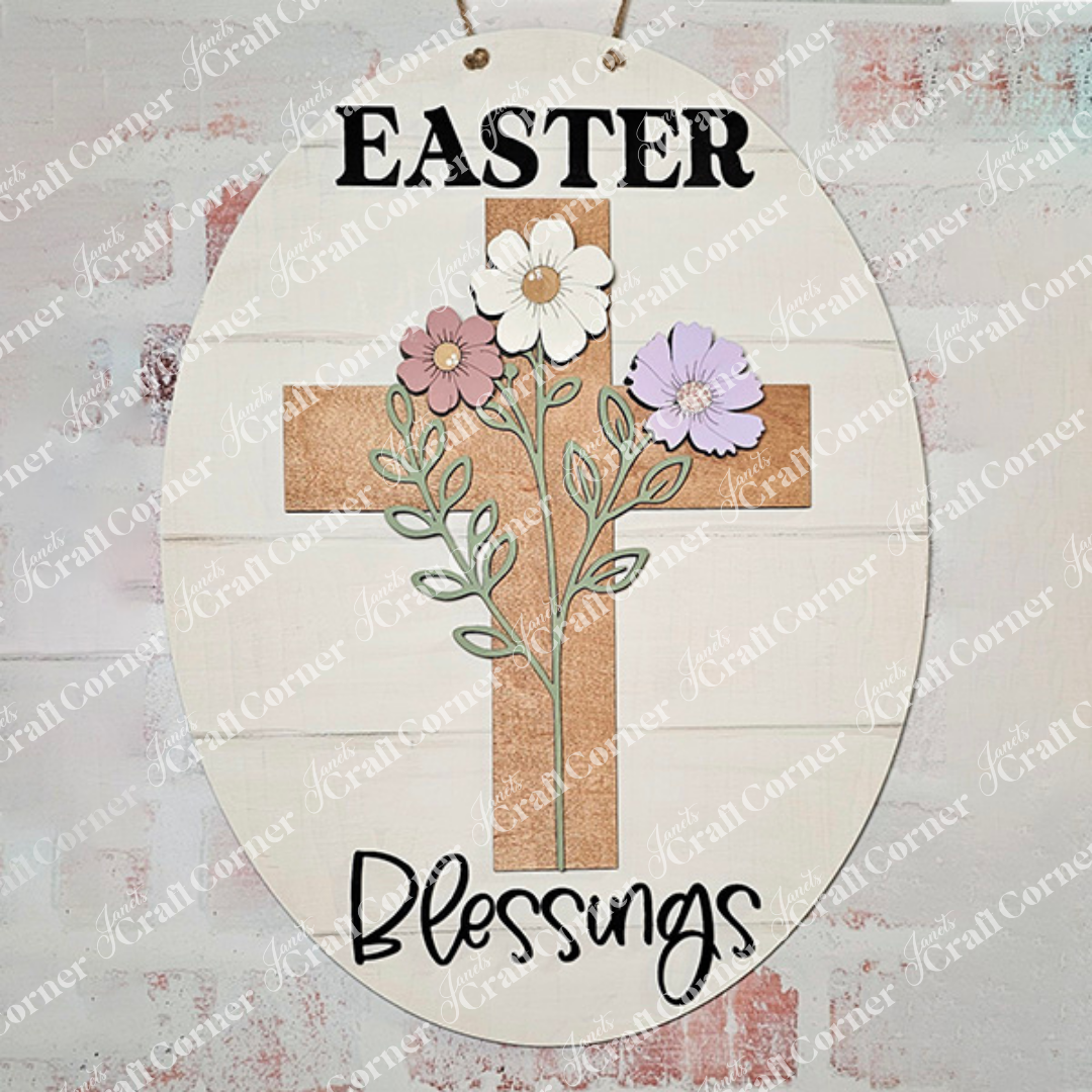 The Easter Blessings Door Hanger by Janet's Craft Corner features a white oval sign with a floral cross wood cut-out design. It includes three flowers with green stems and the words "Easter" and "Blessings" on a light wood textured background, ideal for DIY seasonal home decor.