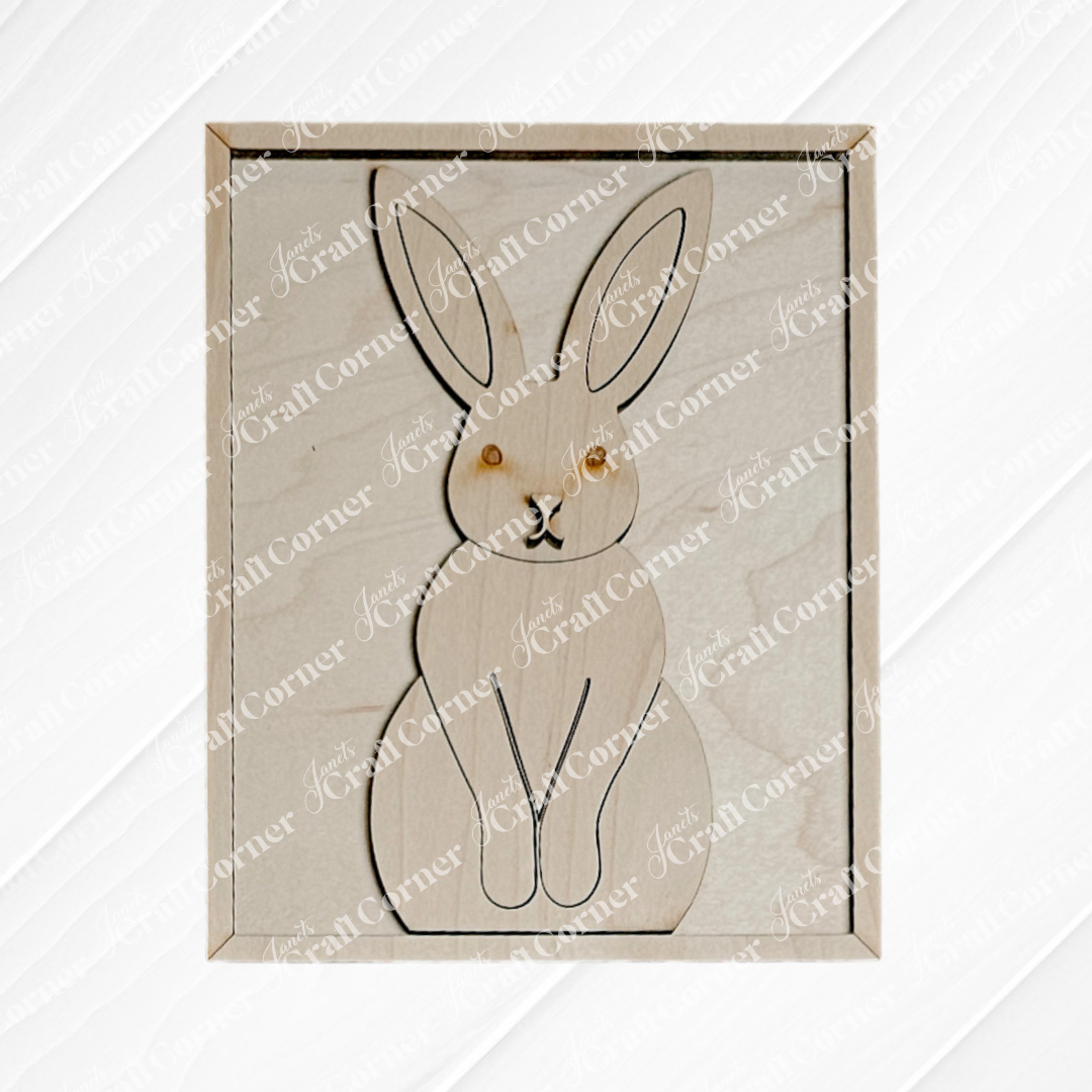 The Easter Bunny Farmhouse Sign by Janet's Craft Corner is a wood cut-out frame with a silhouette of a sitting rabbit with large ears, black outlines, and small brown eyes. It features a subtly textured background, perfect for DIY seasonal home decor.