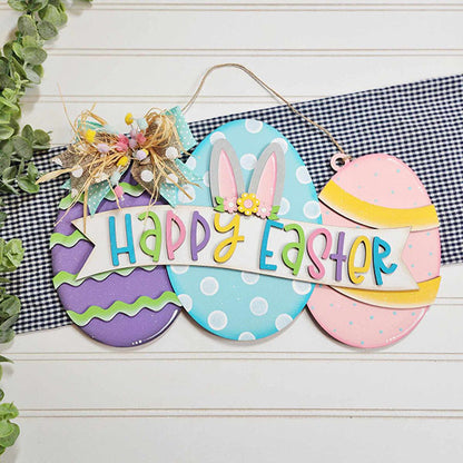 The Easter Egg Sign by Janet's Craft Corner features a trio of egg designs decorated with vibrant patterns and a cheerful "Happy Easter" message. It is embellished with charming bunny ears, flowers, and a gingham ribbon, perfectly complementing your Easter décor against a checkered background enhanced by green foliage accents.