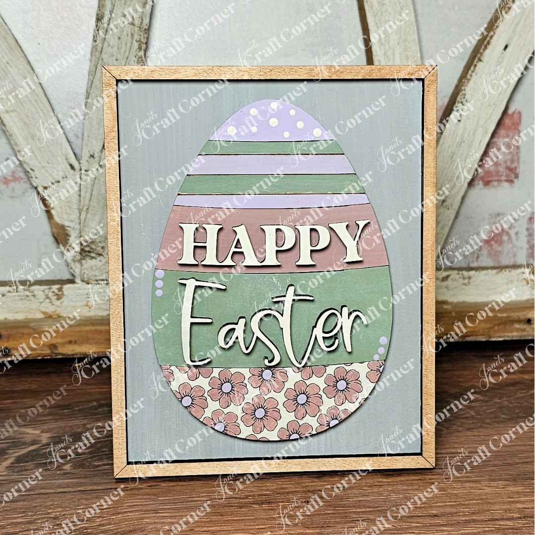 The Easter Egg Farmhouse Sign by Janet's Craft Corner is a DIY craft kit featuring a framed egg with pastel green, pink, and purple stripes, floral patterns, and "Happy Easter." It includes wood cut-outs and a wooden border frame, ideal for seasonal home decor enthusiasts.