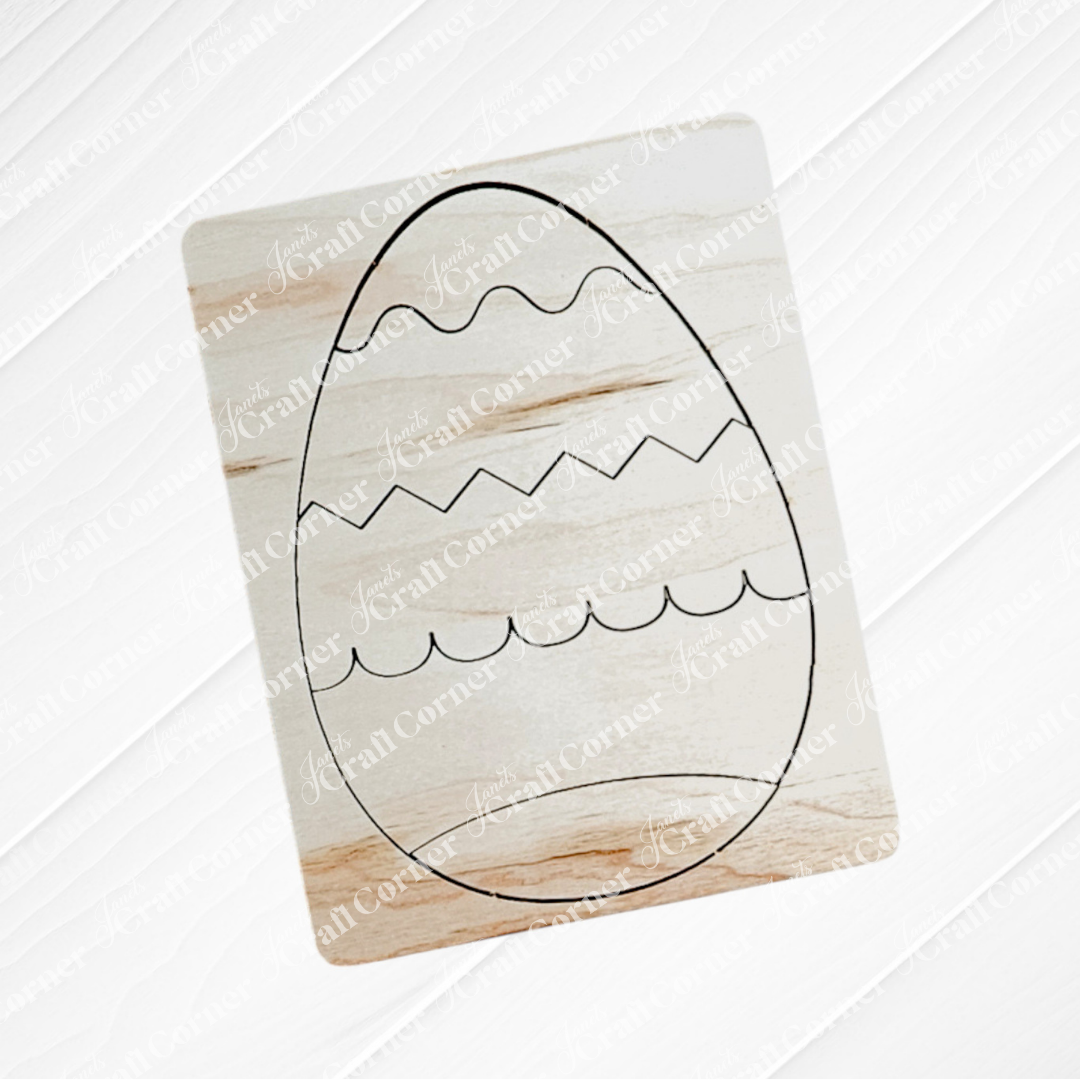 The Easter Egg Pop Out Puzzle by Janet's Craft Corner is a wooden square ideal for DIY home decor, featuring a laser-cut egg with wavy lines and zigzags, complemented by the wood's light natural finish and a subtle diagonal pattern.