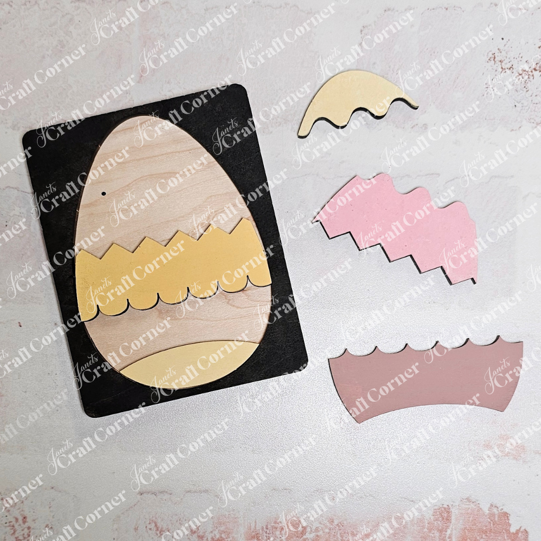 Janet's Craft Corner offers the Easter Egg Pop Out Puzzle, a craft kit for making an egg-shaped card with zigzag patterns. It includes a black base, tan oval, and separate pink, yellow, and tan zigzag pieces on a textured white background—ideal for DIY home decor enthusiasts.