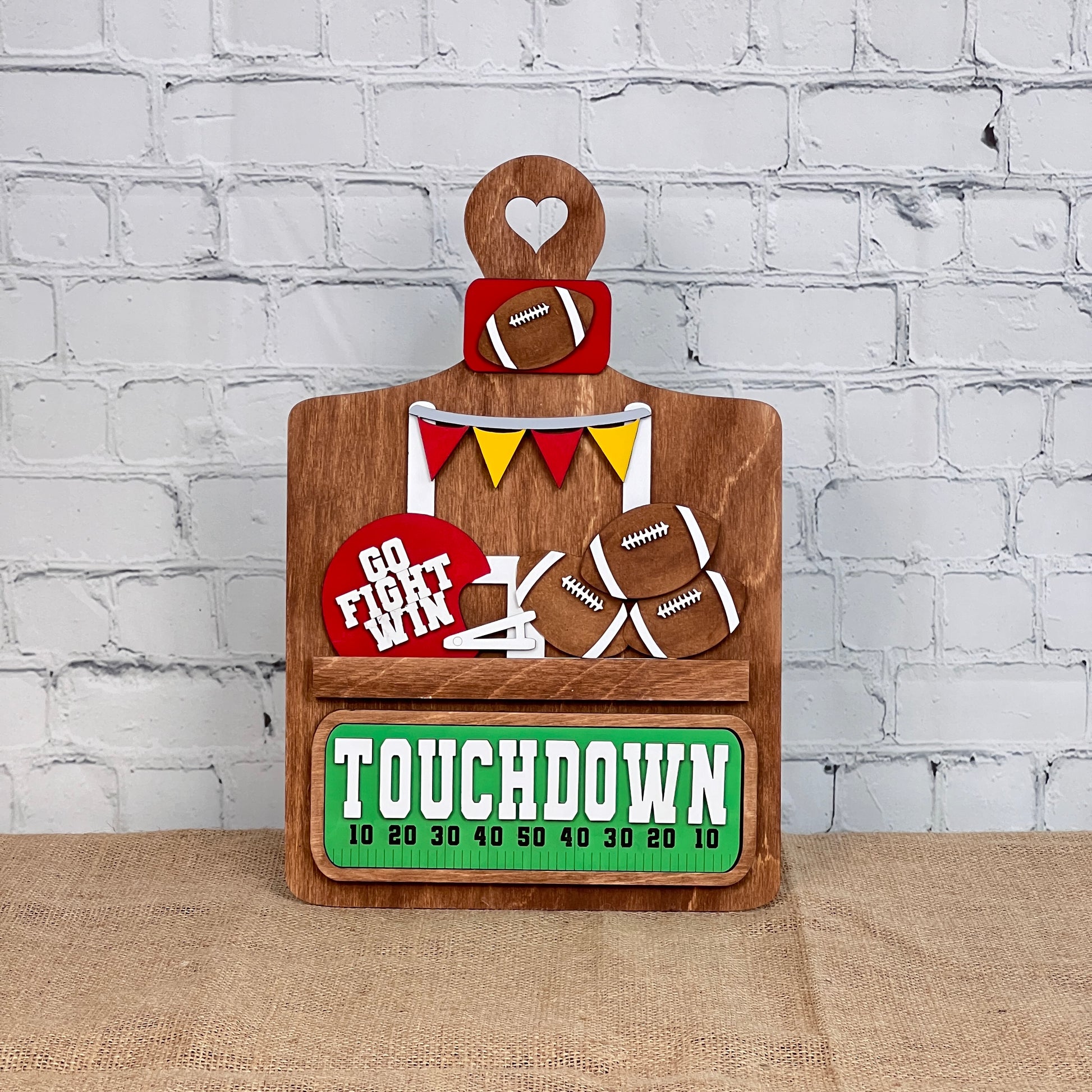 The Breadboard Interchangeable Base with Insert by Janet's Craft Corner offers a wooden football-themed DIY decor kit featuring a "TOUCHDOWN" scoreboard, mini footballs, colorful banners, and "GO FIGHT WIN" on red. Perfect for rustic charm against white brick and burlap surfaces.