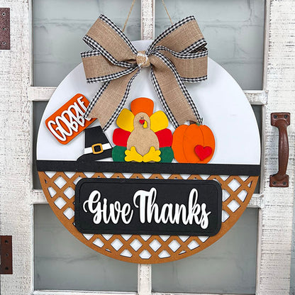 Janet's Craft Corner's Door Hanger Interchangeable Base with Insert features a Thanksgiving design with a turkey, pumpkin, and witch's hat. Adorned with "Gobble" and "Give Thanks" text and topped with a burlap and gingham bow, this DIY decor kit adds seasonal charm to your door.