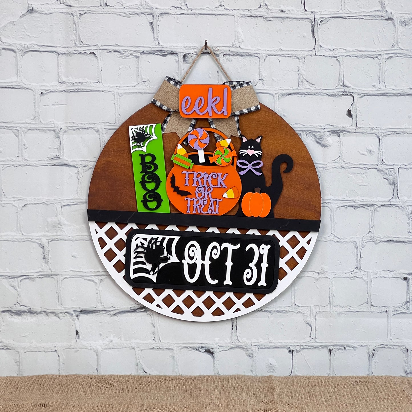 The DIY Door Hanger Interchangeable Base from Janet's Craft Corner is perfect for Halloween décor. It features a pumpkin, black cat, and phrases like "EEK!" and "Trick or Treat" against a brick background, with "Oct 31" displayed. Ideal for creative enthusiasts.