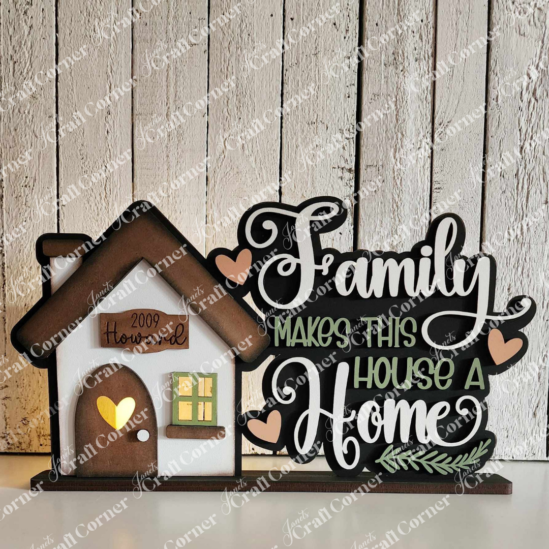 The Family Home Word Art Votive Holder Shelf Sitter from Janet's Craft Corner features a small house with a brown roof and window. It has "Family makes this house a home" in elegant lettering adorned with hearts, plus "2009" on the textured white background for charm.