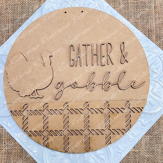 The Gather & Gobble Door Hanger by Janet's Craft Corner showcases a round wooden sign adorned with a turkey silhouette and the phrase "Gather & Gobble." Enhanced by a woven mat pattern beneath, this DIY home décor craft kit is ideal for adorning your space. Its textured burlap background makes it an excellent wall hanger for fall festivities.