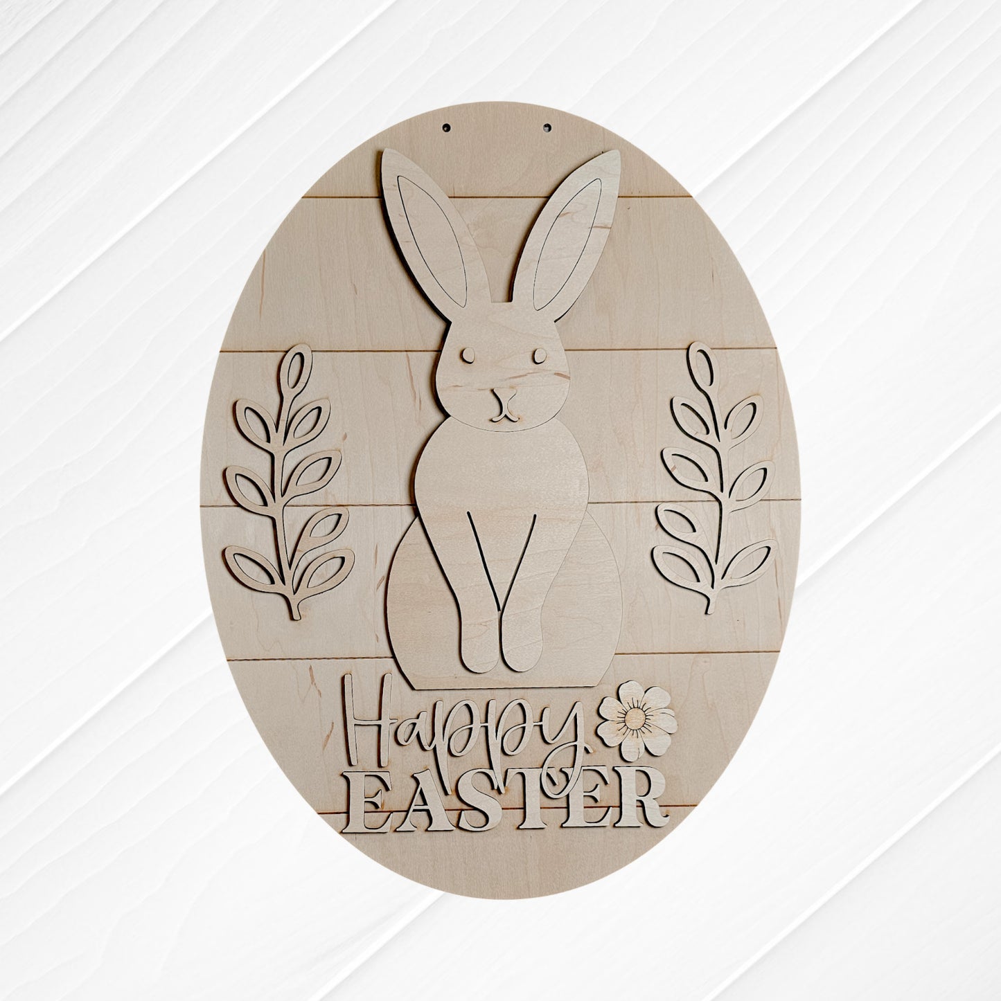 The Happy Easter Door Hanger from Janet's Craft Corner is a DIY home decor piece featuring a carved rabbit and floral designs. It has "Happy Easter" text at the bottom, is oval-shaped with a white, textured background—ideal for any wood cut-out collection.