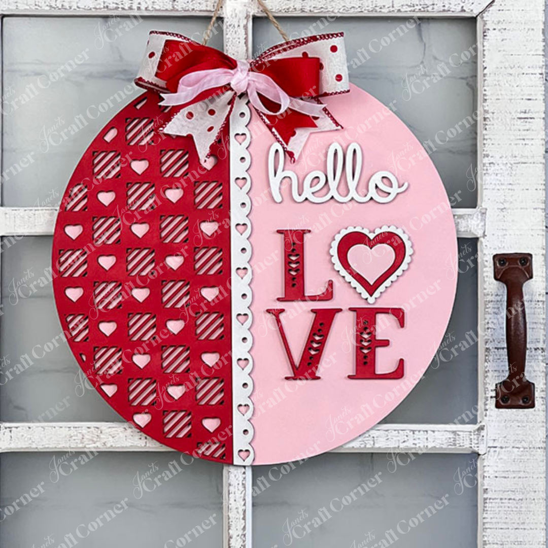 Introducing Janet's Craft Corner's "Hello Love Round Sign" DIY Kit: Delight in creating a beautiful piece of home decor that's perfect for Valentine's Day. This round sign features a sophisticated "hello LOVE" script, with the left half displaying a vibrant red hue adorned with heart patterns and the right half in a soft pink shade. It is elegantly finished with a charming red and white bow.