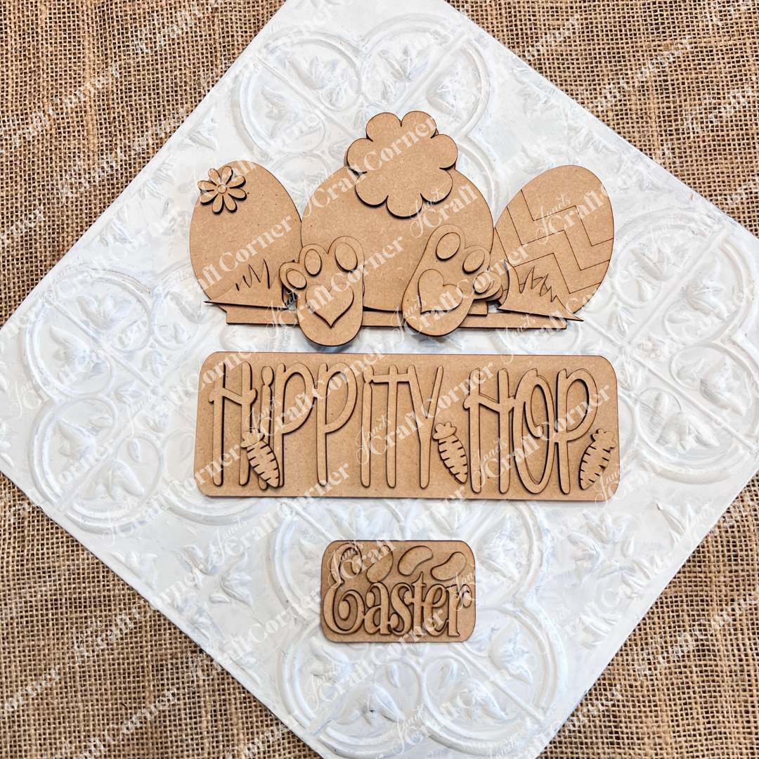 The "Hippity Hop Bunny Butt Interchangeable Insert" by Janet's Craft Corner is a charming hand-painted Easter sign on burlap featuring a bunny, patterned eggs, "HIPPITY HOP" with carrots, and "Easter" on a white diamond texture, perfect for DIY crafters seeking versatile home decor.