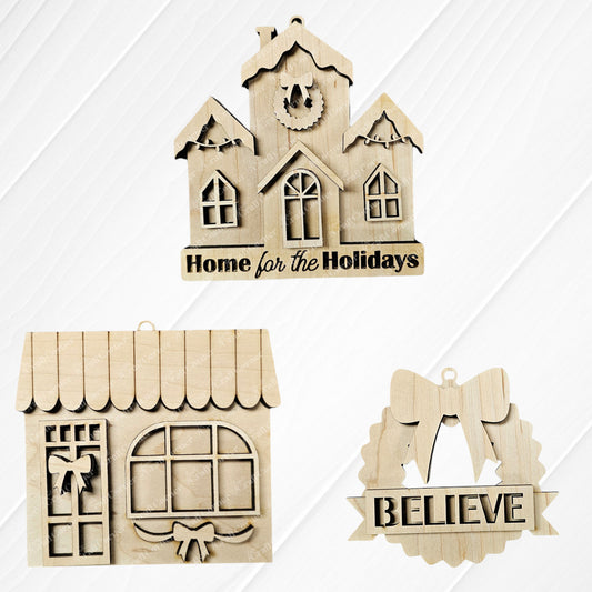 Three wooden ornaments from Janet's Craft Corner's Holiday Village Ornament Set feature: a house with "Home for the Holidays," a window with wreath, and a bow wreath with "BELIEVE." Ideal for your holiday village collection or festive décor on a wood-textured background.