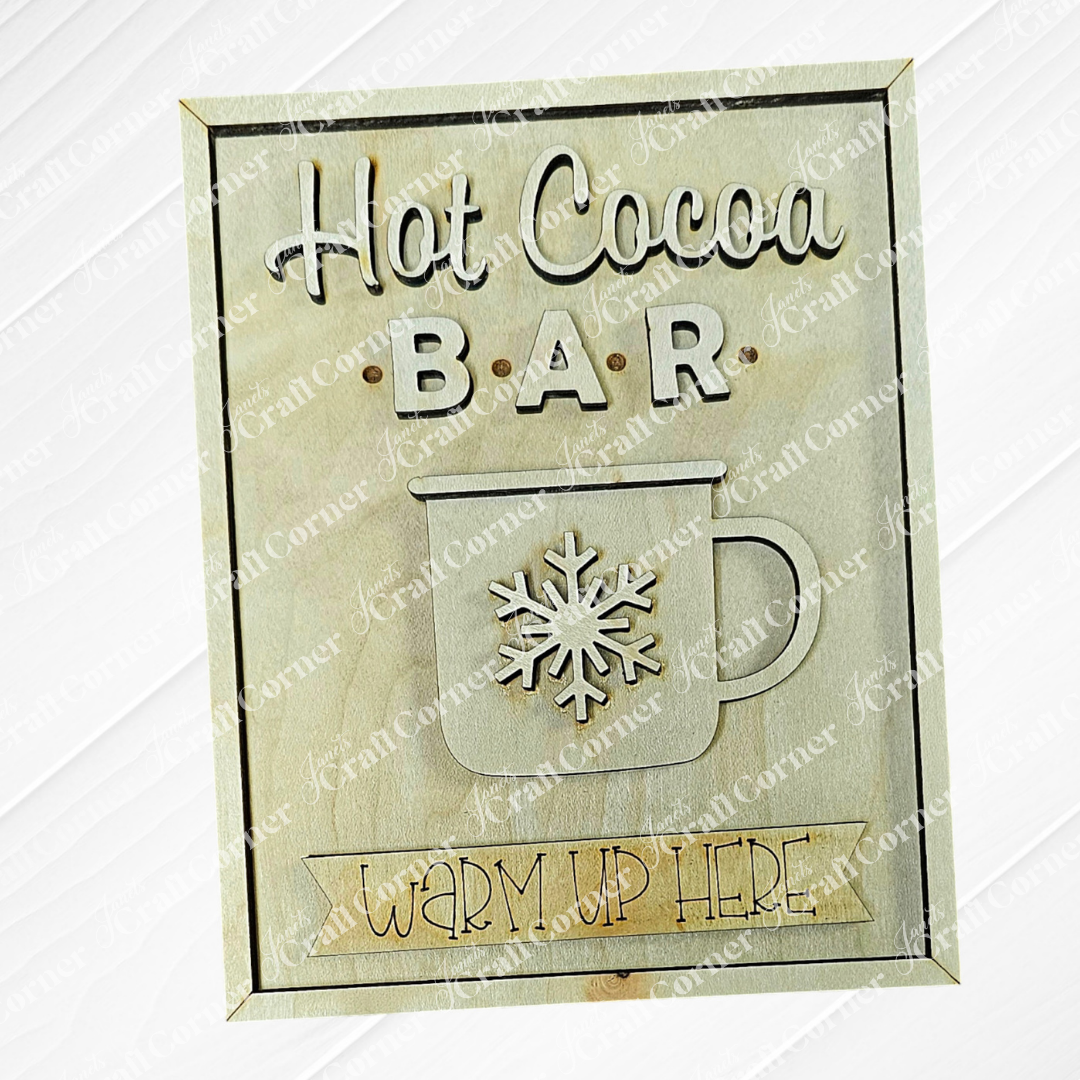 The "Hot Cocoa Bar Interchangeable Sign" by Janet's Craft Corner is a rustic wooden piece, showcasing a charming mug with a snowflake. It warmly invites you to "Warm Up Here," making it ideal for your DIY craft kit collection or to cozy up any space.