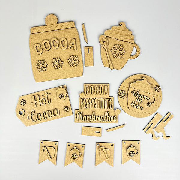 The Hot Cocoa Decor Set by Janet's Craft Corner is a DIY seasonal home decor kit featuring 6 wooden cutouts, including mugs, snowflakes, "Cocoa" tags, tiny skates, and snowflake banners. Ideal for creating a festive Hot Cocoa Tiered Tray display.